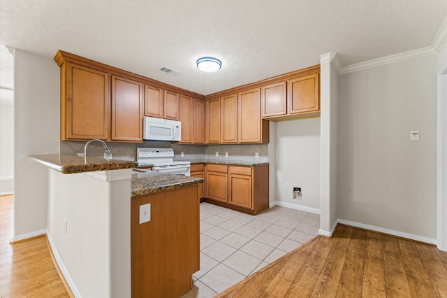 14607 Dawn Mist Ct, Magnolia, TX 77354 - kitchen featuring white appliances, brown cabinetry, a peninsula, backsplash, and dark stone counters