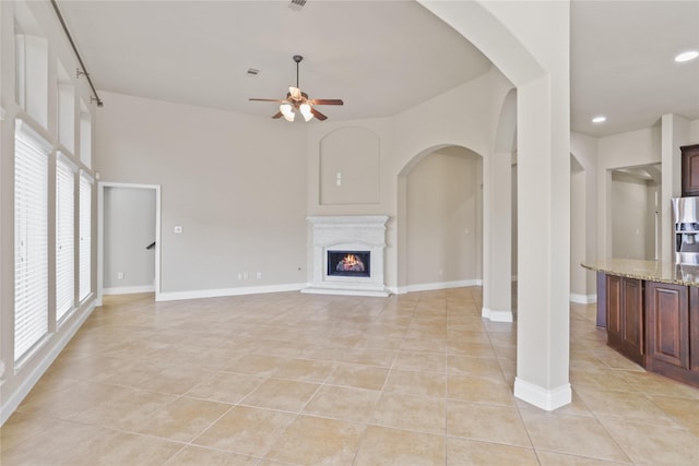 21902 Juniper Wood Ln, Richmond, TX 77469 - unfurnished living room featuring light tile patterned flooring, ceiling fan, arched walkways, a warm lit fireplace, and recessed lighting