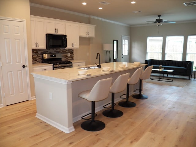 4218 Sorsby Dr, Houston, TX 77047 - kitchen featuring black microwave, stainless steel range with gas cooktop, ornamental molding, white cabinets, and light wood-style flooring