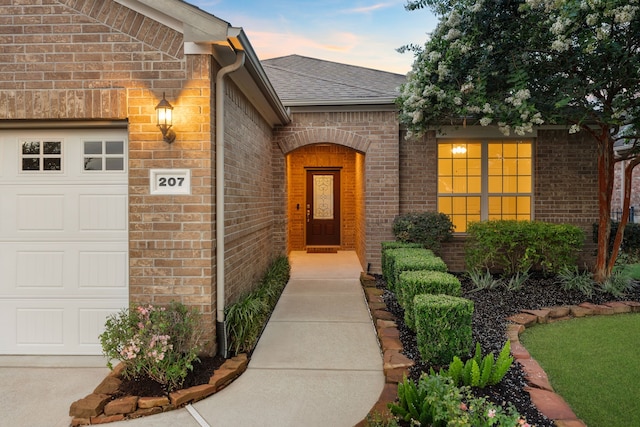 207 Cattle Ranch Dr, Richmond, TX 77469 - exterior entry at dusk featuring an attached garage, brick siding, and roof with shingles