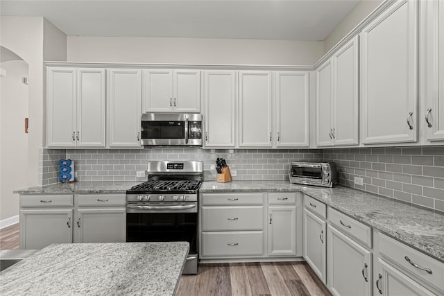 2922 Muhley St, Katy, TX 77493 - kitchen with appliances with stainless steel finishes, arched walkways, light wood-type flooring, and white cabinetry