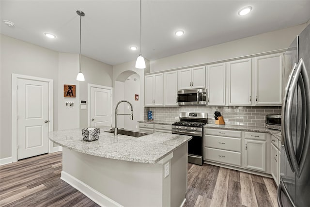2922 Muhley St, Katy, TX 77493 - kitchen with appliances with stainless steel finishes, backsplash, wood finished floors, a kitchen island with sink, and arched walkways