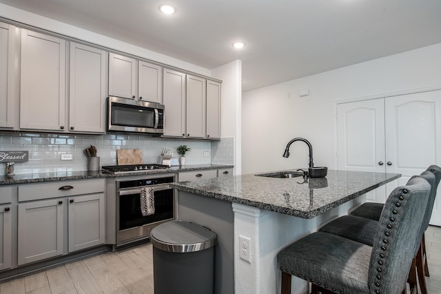 8023 Royal Palm Dr, Fulshear, TX 77441 - kitchen featuring appliances with stainless steel finishes, gray cabinetry, dark stone counters, tasteful backsplash, and a breakfast bar area