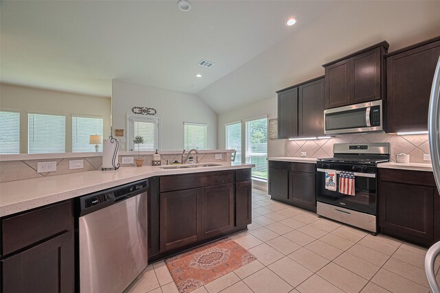 406 Riesling Dr, Alvin, TX 77511 - kitchen featuring appliances with stainless steel finishes, decorative backsplash, vaulted ceiling, dark brown cabinetry, and light tile patterned flooring