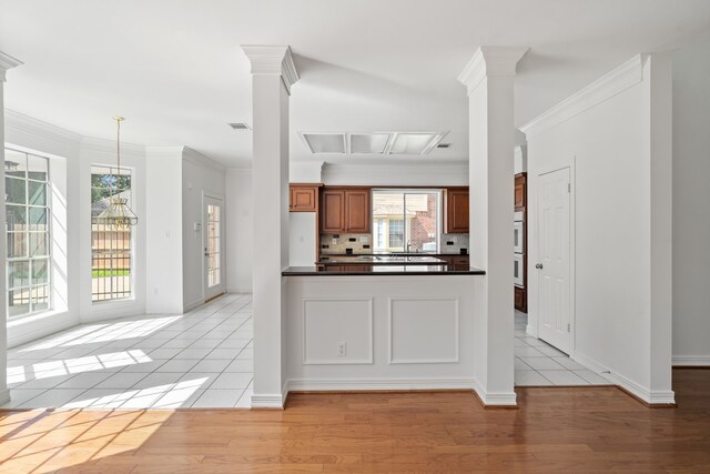 4919 Glen Hollow St, Sugar Land, TX 77479 - kitchen with dark countertops, light wood-type flooring, decorative columns, brown cabinetry, and crown molding