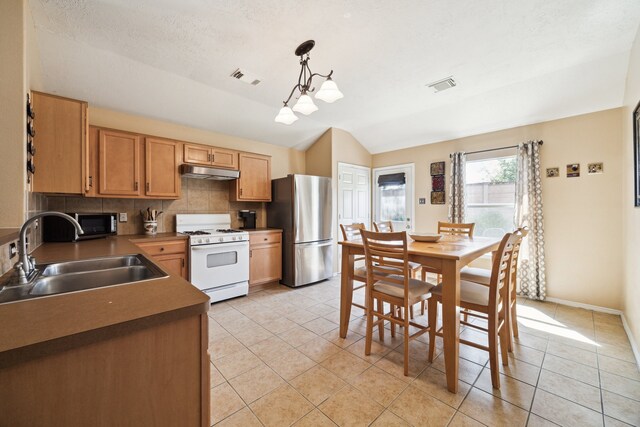 7238 Cypress Prairie Dr, Cypress, TX 77433 - kitchen with stainless steel appliances, under cabinet range hood, vaulted ceiling, light tile patterned floors, and decorative backsplash