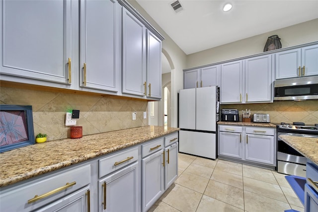 66 N Rocky Point Cir, Spring, TX 77389 - kitchen featuring appliances with stainless steel finishes, arched walkways, tasteful backsplash, light tile patterned floors, and light stone countertops