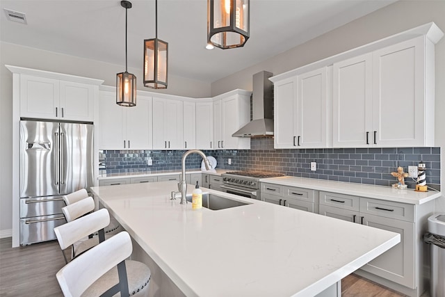 3914 Curlew Dr, Galveston, TX 77554 - kitchen featuring high quality appliances, wall chimney range hood, wood finished floors, an island with sink, and backsplash