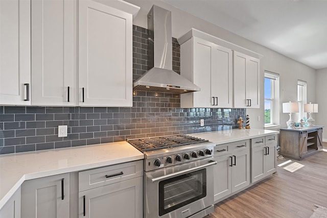 3914 Curlew Dr, Galveston, TX 77554 - kitchen with wall chimney exhaust hood, high end stove, light wood-type flooring, tasteful backsplash, and light stone countertops