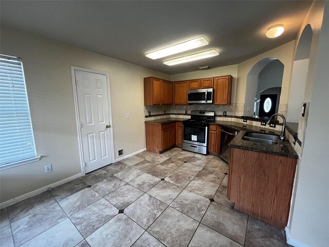 6830 Silver Shores Ln, Katy, TX 77449 - kitchen featuring stainless steel appliances, brown cabinetry, backsplash, dark stone counters, and arched walkways