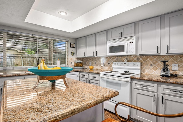 5427 Cairnleigh Dr, Houston, TX 77084 - kitchen featuring white appliances, decorative backsplash, light stone countertops, gray cabinets, and a tray ceiling