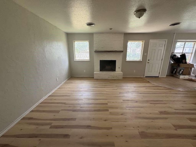5431 45th St, Lubbock, TX 79414 - unfurnished living room featuring light wood finished floors, a textured ceiling, a textured wall, and a fireplace