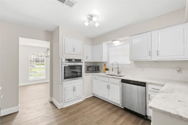 3101 Possum Trot St, Brenham, TX 77833 - kitchen featuring stainless steel appliances, white cabinets, light wood-style flooring, decorative backsplash, and light stone countertops