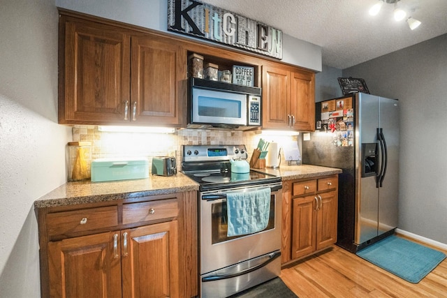 1501 Wimbledon Dr, Huntsville, TX 77340 - kitchen with stainless steel appliances, brown cabinetry, light wood-style flooring, tasteful backsplash, and a textured ceiling
