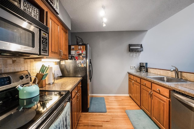 1501 Wimbledon Dr, Huntsville, TX 77340 - kitchen featuring appliances with stainless steel finishes, decorative backsplash, brown cabinets, light wood-type flooring, and a textured ceiling