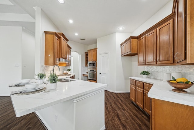 25207 Oak Star Dr, Spring, TX 77389 - kitchen featuring a peninsula, arched walkways, dark wood-style flooring, brown cabinets, and recessed lighting