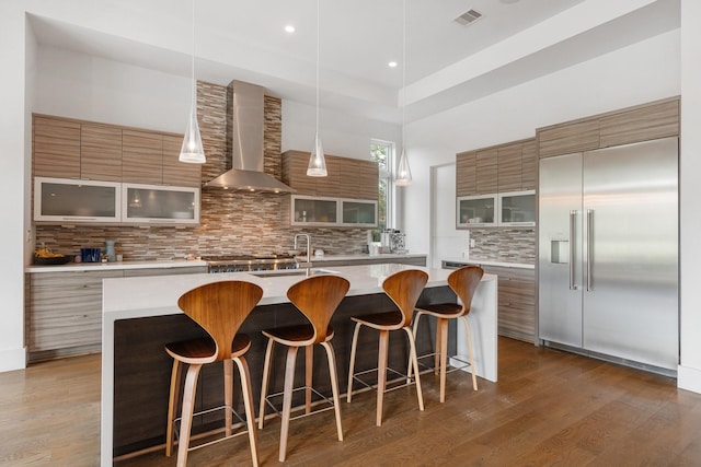 18 Pronghorn Pl, The Woodlands, TX 77389 - kitchen with wall chimney exhaust hood, built in fridge, modern cabinets, backsplash, and a center island with sink