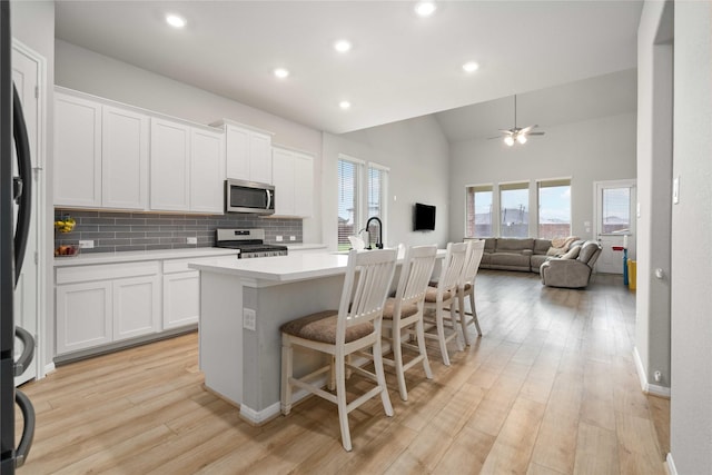13402 Rain Lily, Texas City, TX 77568 - kitchen featuring appliances with stainless steel finishes, lofted ceiling, a center island with sink, white cabinets, and light wood-type flooring