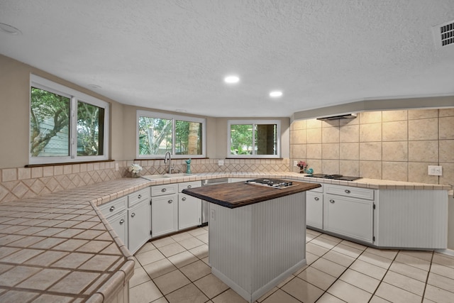 1406 Diana Ct, Houston, TX 77062 - kitchen featuring decorative backsplash, white cabinetry, stainless steel gas stovetop, a textured ceiling, and wood counters