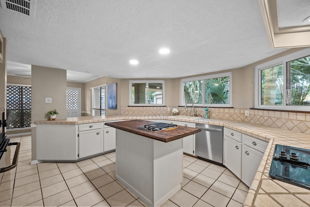 1406 Diana Ct, Houston, TX 77062 - kitchen featuring appliances with stainless steel finishes, tasteful backsplash, white cabinets, light tile patterned floors, and a textured ceiling