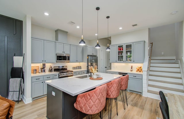 4612 Oats St, Houston, TX 77020 - kitchen with appliances with stainless steel finishes, light wood finished floors, glass insert cabinets, gray cabinets, and a center island with sink