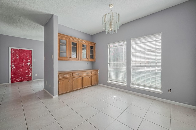 11280 Braes Forest Dr Unit 105, Houston, TX 77071 - kitchen featuring a chandelier, brown cabinets, light tile patterned floors, a textured ceiling, and glass insert cabinets