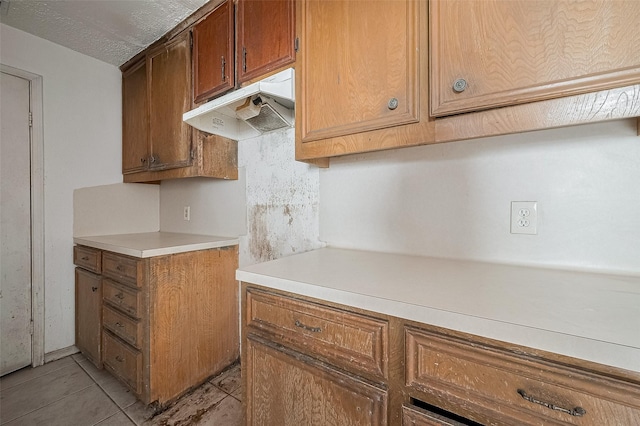11280 Braes Forest Dr Unit 105, Houston, TX 77071 - kitchen featuring under cabinet range hood, light countertops, brown cabinets, and light tile patterned flooring