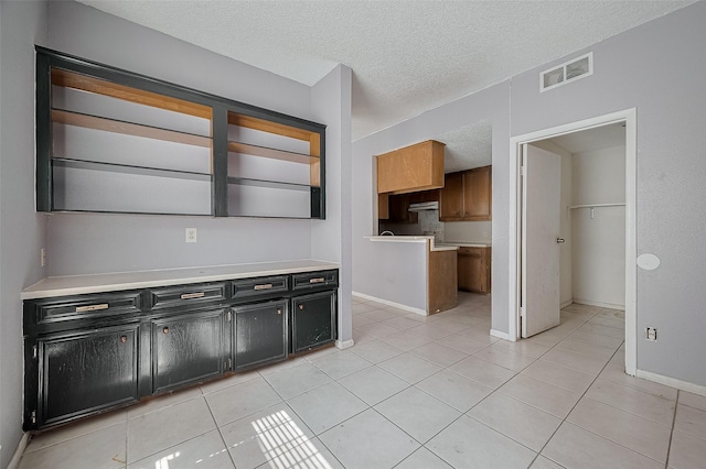 11280 Braes Forest Dr Unit 105, Houston, TX 77071 - kitchen with dark cabinets, a textured ceiling, light tile patterned flooring, under cabinet range hood, and light countertops