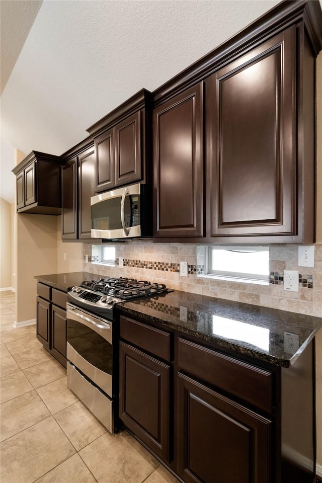 38 Tallgrass Way, Spring, TX 77389 - kitchen featuring stainless steel appliances, dark brown cabinets, decorative backsplash, light tile patterned floors, and dark stone counters