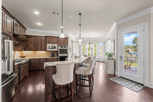 6051 Longmire Trl, Conroe, TX 77304 - kitchen with stainless steel appliances, dark wood-style flooring, decorative backsplash, a center island with sink, and light stone countertops