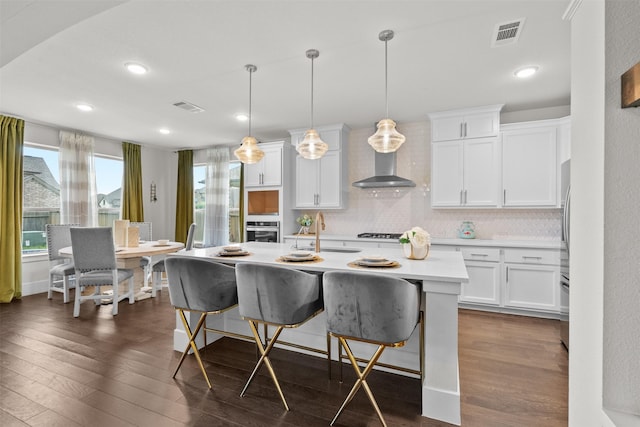 27915 Round Moon Ln, Katy, TX 77494 - kitchen with stainless steel oven, dark wood finished floors, a kitchen bar, backsplash, and light countertops