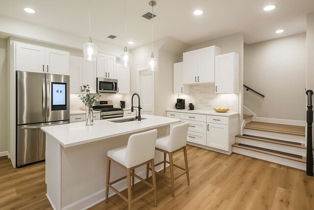 2353 Hoskins Dr, Houston, TX 77080 - kitchen featuring stainless steel appliances, light wood finished floors, an island with sink, decorative backsplash, and white cabinets