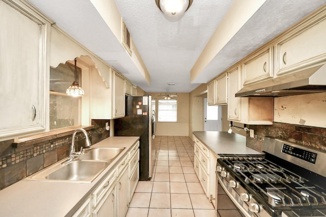 30718 N Cripple Creek Dr, Magnolia, TX 77354 - kitchen with stainless steel gas range, cream cabinetry, exhaust hood, decorative backsplash, and light tile patterned floors