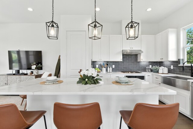 3913 Hare St, Houston, TX 77020 - kitchen featuring under cabinet range hood, decorative backsplash, a kitchen breakfast bar, white cabinets, and recessed lighting