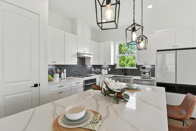 3913 Hare St, Houston, TX 77020 - kitchen with stainless steel appliances, under cabinet range hood, decorative backsplash, pendant lighting, and white cabinetry