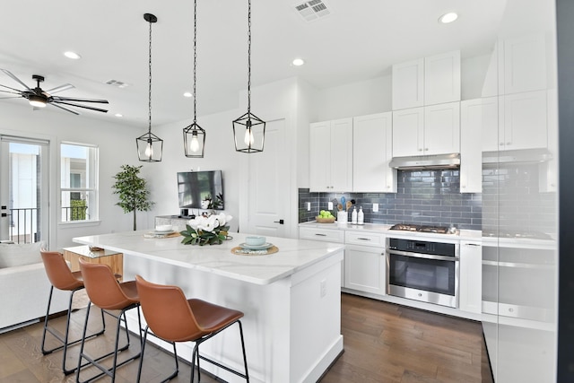 3913 Hare St, Houston, TX 77020 - kitchen with stainless steel appliances, a kitchen island, backsplash, dark wood finished floors, and white cabinetry