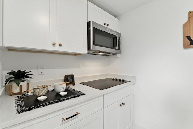 3913 Hare St, Houston, TX 77020 - kitchen featuring stainless steel microwave, black electric stovetop, white cabinets, and light countertops