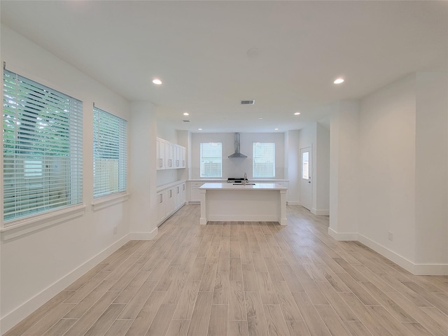 6735 Cohn St, Houston, TX 77091 - kitchen featuring wall chimney range hood, light wood-type flooring, light countertops, a center island with sink, and white cabinetry