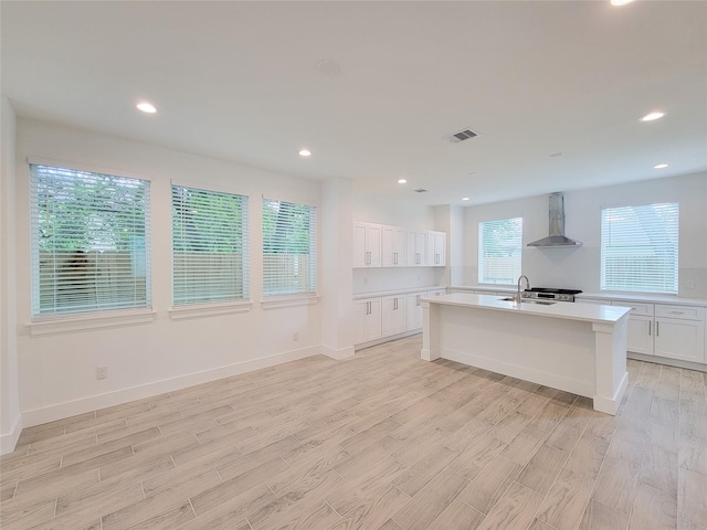 6735 Cohn St, Houston, TX 77091 - kitchen with wall chimney range hood, light countertops, light wood-type flooring, an island with sink, and recessed lighting