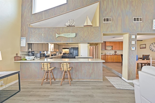 206 Galleon Dr, Freeport, TX 77541 - kitchen with a high ceiling, black fridge, a peninsula, light wood-style flooring, and a breakfast bar area