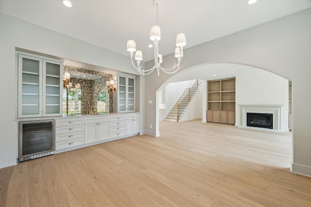 2006 Chantilly Ln, Houston, TX 77018 - unfurnished living room featuring wine cooler, a chandelier, arched walkways, light wood finished floors, and stairs