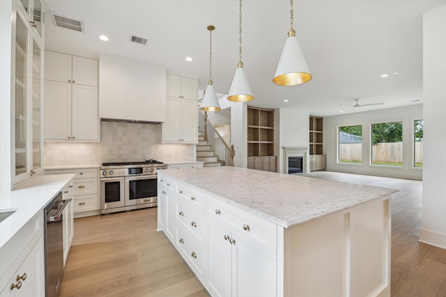 2006 Chantilly Ln, Houston, TX 77018 - kitchen featuring appliances with stainless steel finishes, a center island, a fireplace, light wood-style flooring, and decorative backsplash