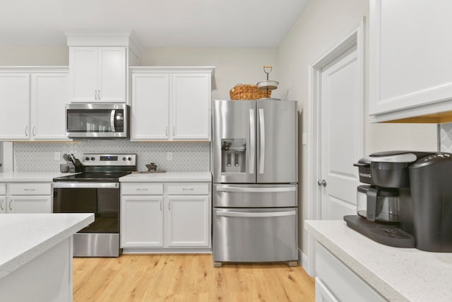16003 Westward Ho St, Stagecoach, TX 77355 - kitchen featuring appliances with stainless steel finishes, white cabinets, decorative backsplash, light wood-type flooring, and light stone countertops