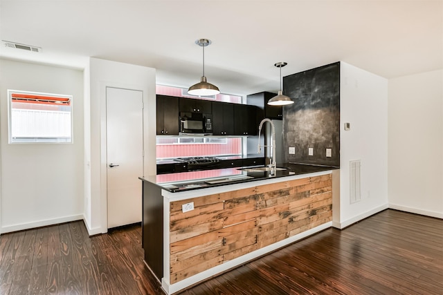 3028 Commerce St, Houston, TX 77003 - kitchen with black microwave, dark wood-type flooring, a peninsula, decorative light fixtures, and dark countertops