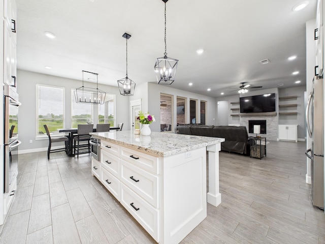 2711 Oakwood Shores Dr, Richwood, TX 77515 - kitchen with stainless steel appliances, ceiling fan, a fireplace, light stone counters, and a kitchen island