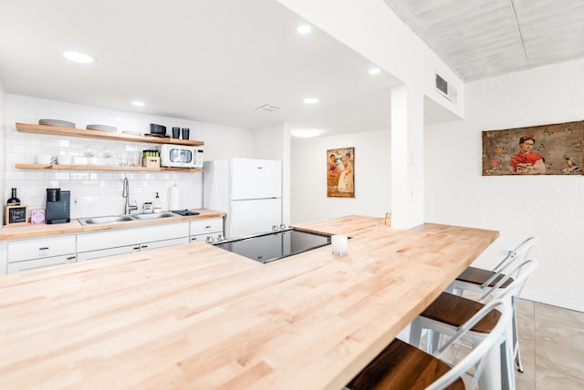 14401 Commodores Dr Unit 104, Corpus Christi, TX 78418 - kitchen with white appliances, butcher block counters, white cabinetry, backsplash, and a breakfast bar area