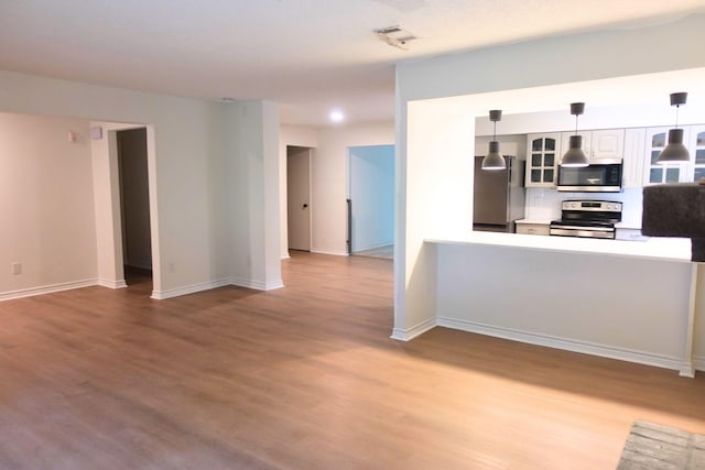 12227 Gun Oak Pl, The Woodlands, TX 77380 - kitchen with stainless steel appliances, glass insert cabinets, wood finished floors, pendant lighting, and white cabinetry