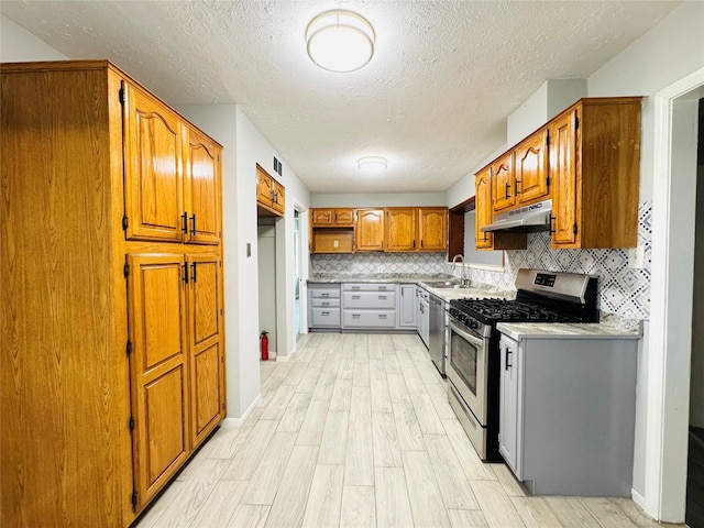7905 Turquoise Ln, Houston, TX 77055 - kitchen featuring appliances with stainless steel finishes, under cabinet range hood, light wood finished floors, brown cabinetry, and a textured ceiling