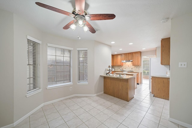 8602 Canyon Pine Dr, Spring, TX 77379 - kitchen with a peninsula, under cabinet range hood, ceiling fan, tasteful backsplash, and brown cabinetry