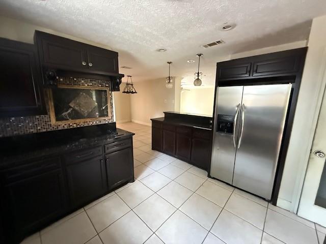 5914 Foresthaven Dr, Houston, TX 77066 - kitchen with stainless steel refrigerator with ice dispenser, dark cabinetry, light tile patterned floors, decorative backsplash, and a textured ceiling